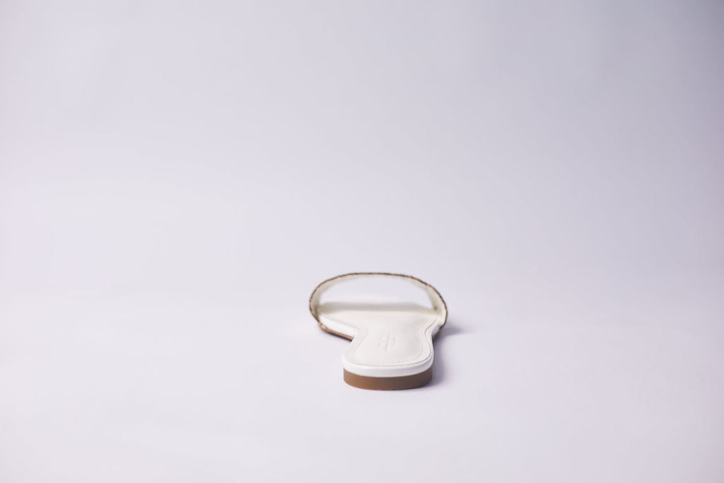 A single white flat sandal shown from the back on a seamless light gray studio background.