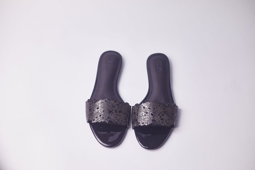 A pair of dark gray slide sandals with metallic silver laser-cut patterned straps, shown from a top-down view on a light gray background.