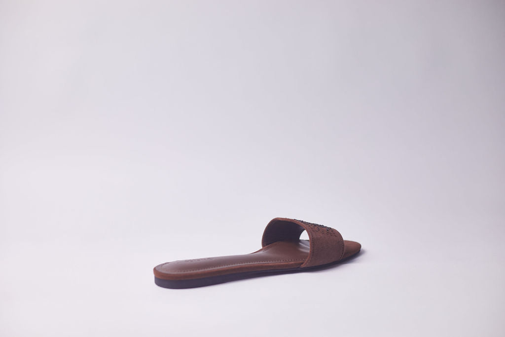 A single brown leather slide sandal with a wide strap and a contoured footbed, photographed from the side against a plain light gray background.
