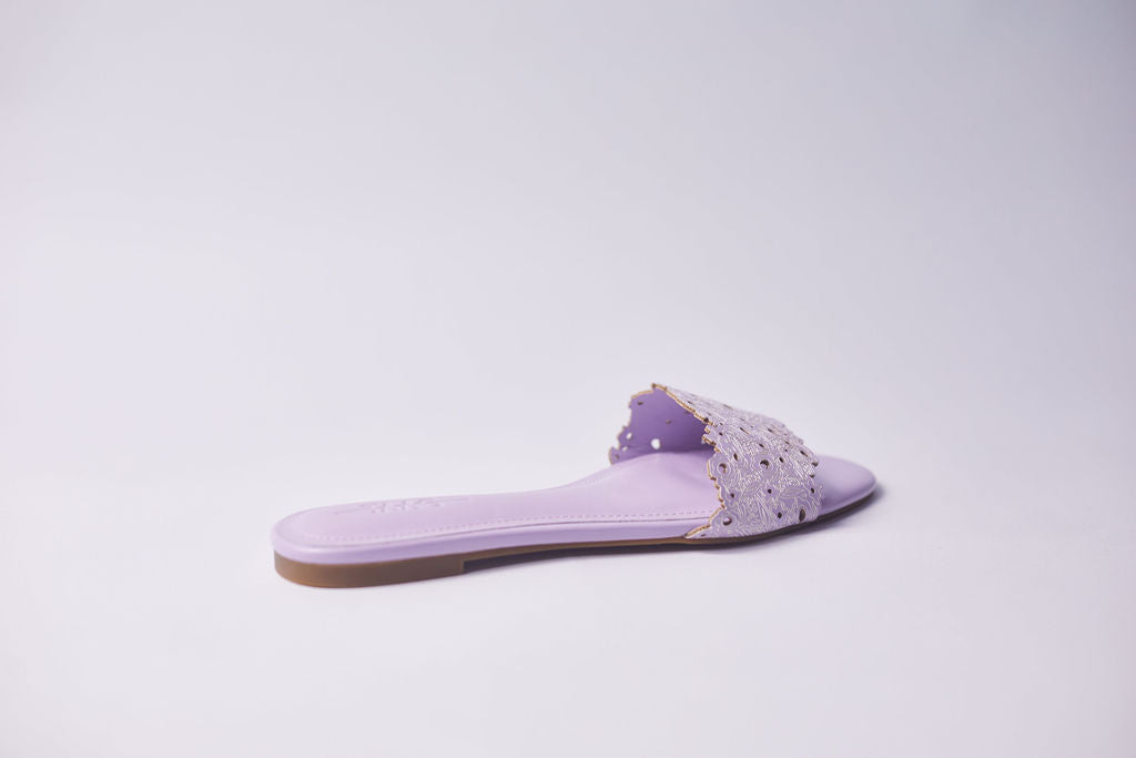 A single lavender purple slide sandal with a textured, perforated strap and a flat sole, shown from a side profile on a light gray background.