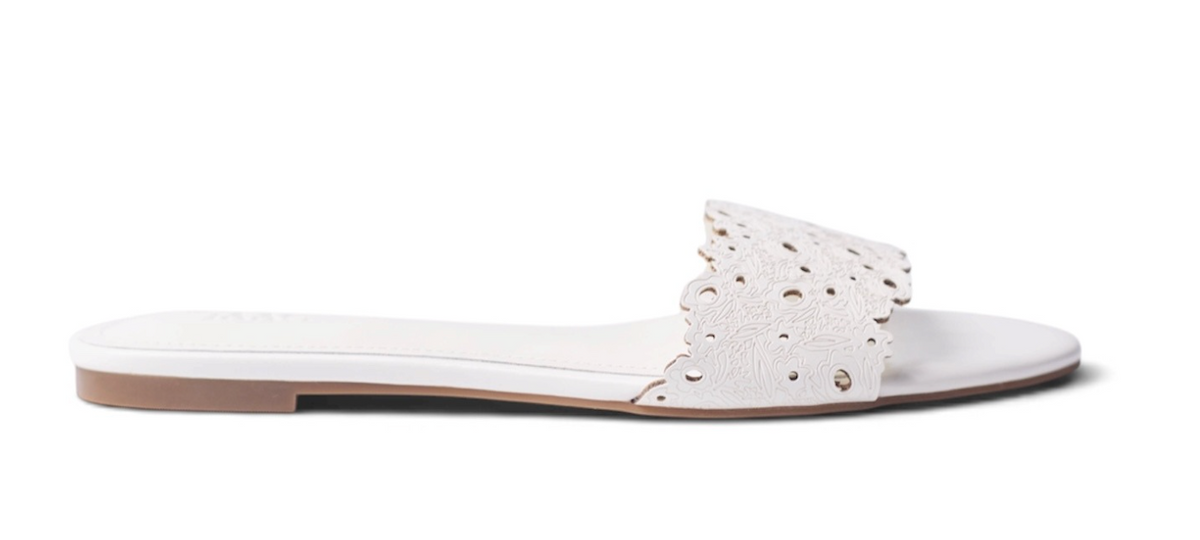 A single white flat slide sandal with a decorative laser-cut strap featuring small rhinestone accents, shown from a side profile on a white background.