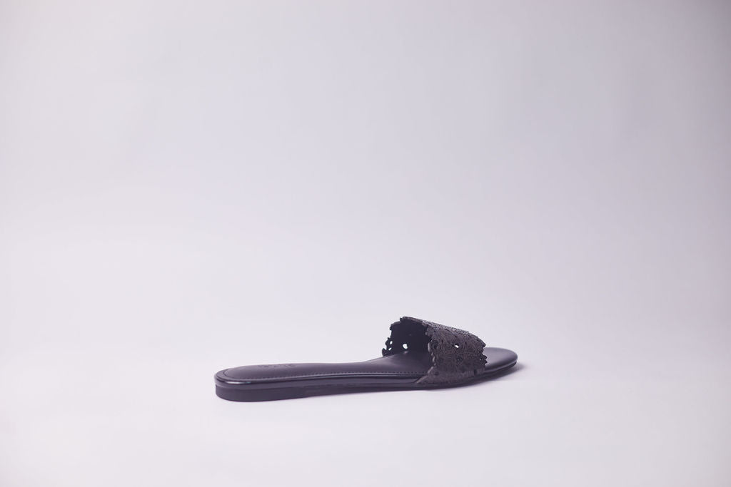 A single dark gray leather slide sandal with a textured, fringed strap, shown from a side profile against a light gray studio background.