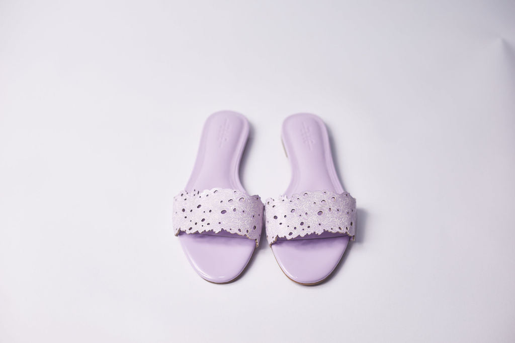 A pair of lavender slide sandals with laser-cut floral straps, displayed on a clean white background.